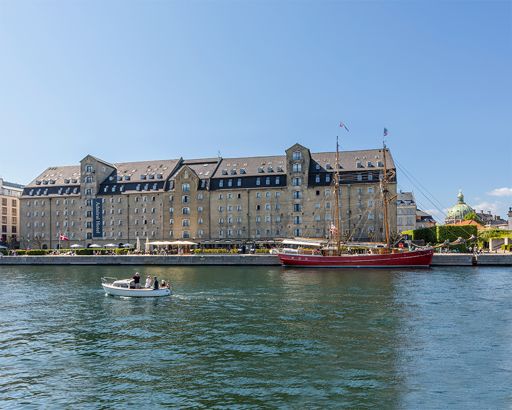 Hotel Admiral fra vandet med rød sejlbåd i forgrunden / Artelia / Rådgivende Ingeniører